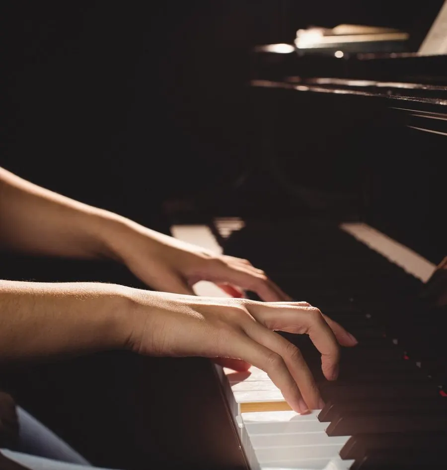 Unas manos tocan el teclado de un piano en penumbra; la luz cae sobre las teclas.
