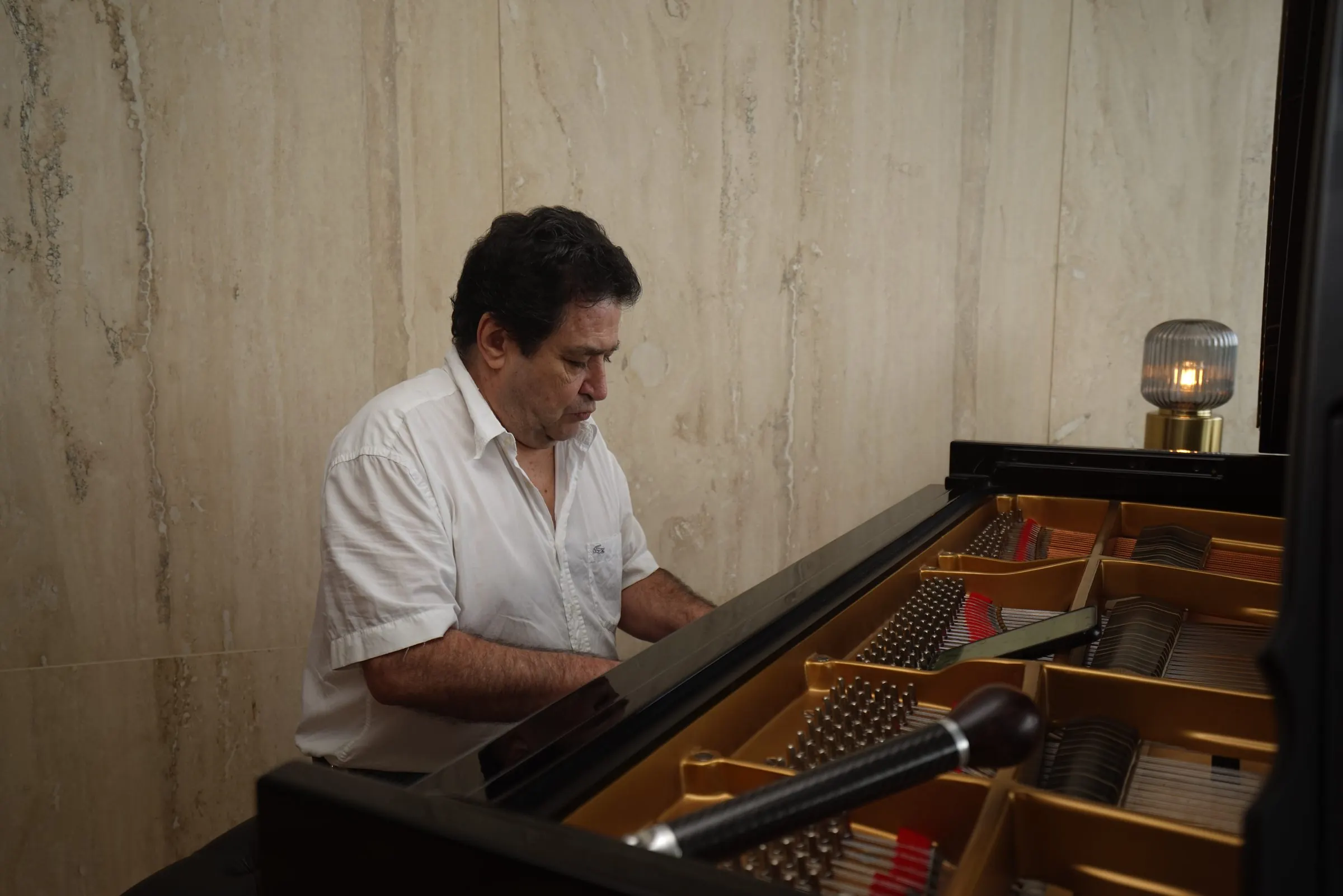 El maestro Rafael Melo toca un piano de cola abierto; la llave de afinar descansa sobre las clavijas.