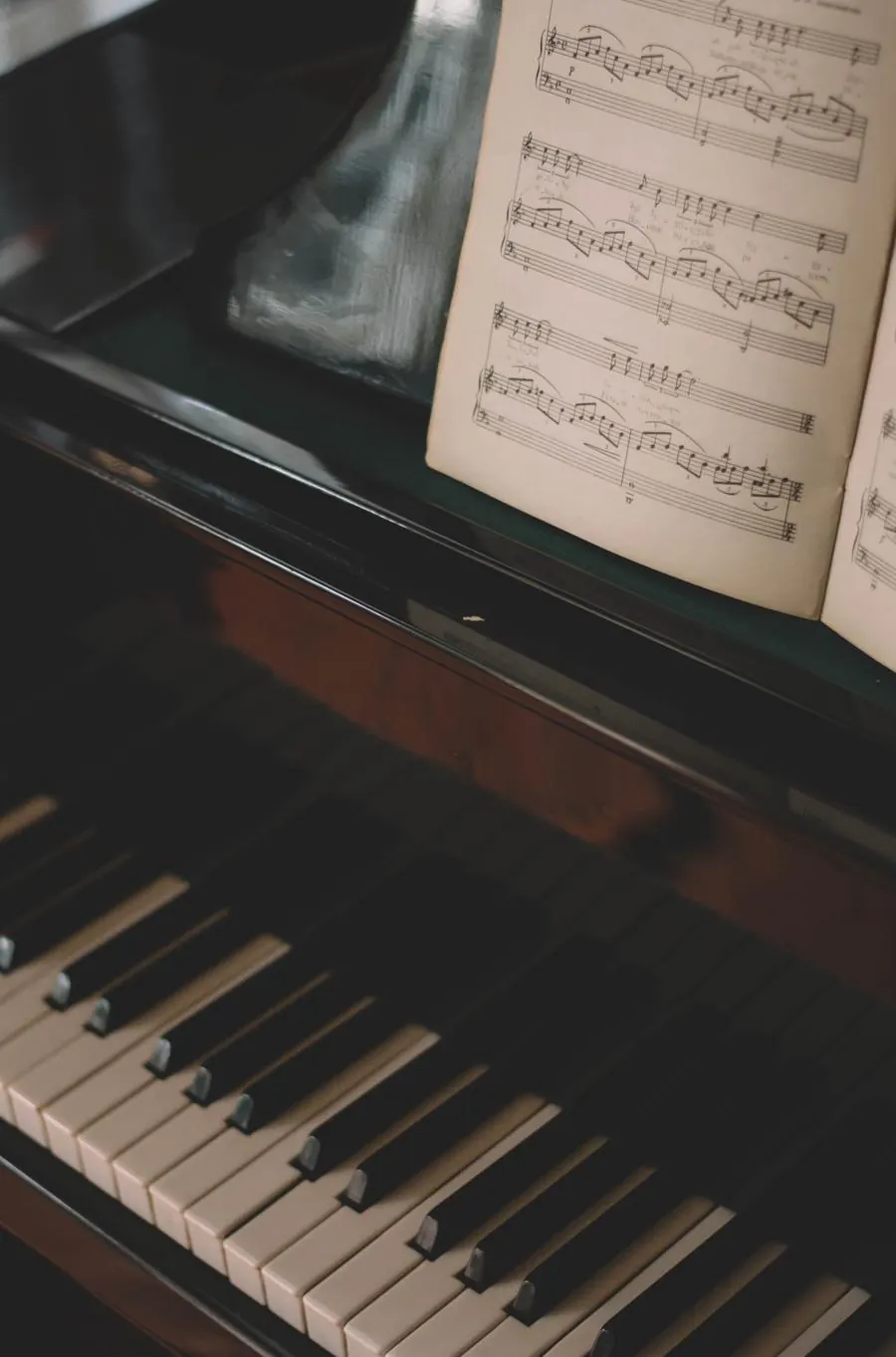 El teclado de un piano en penumbra, con una partitura abierta en el atril.